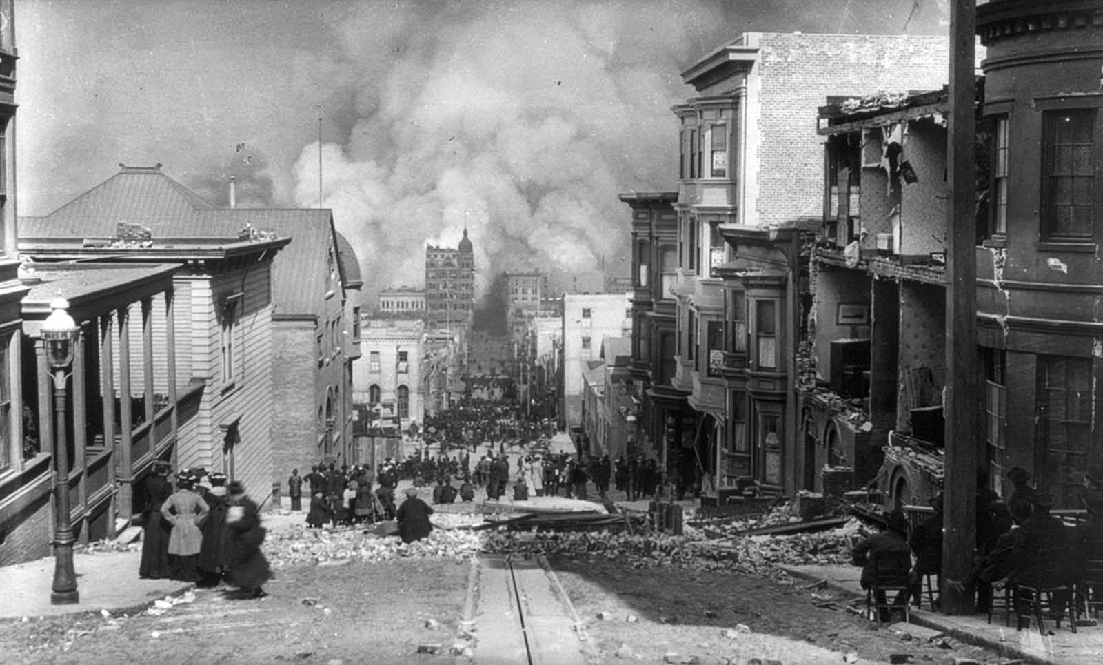 #26 San Francisco residents, some seated in chairs, sit among the earthquake damage, watching out-of-control fires in the distance