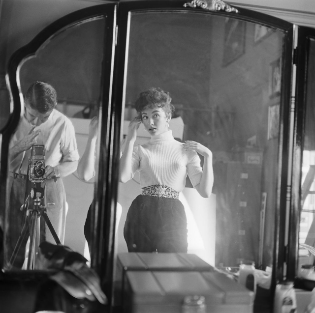 #8 Rita Moreno checking her hair and makeup in the mirror while the photographer prepares to take her photograph, Hollywood, 1954.