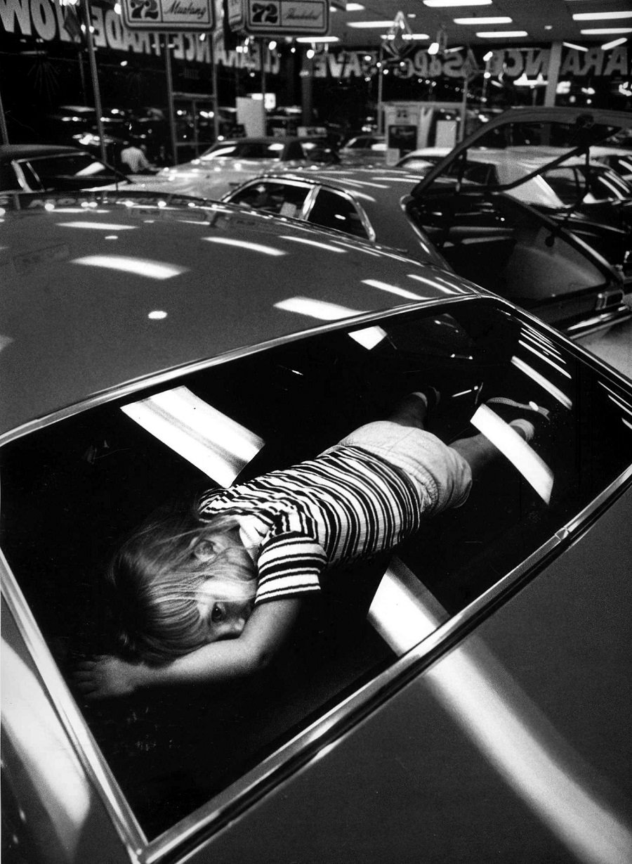 A young girl tries out the “best” seat in a car while her parents shop for one. Atlanta, Georgia, 1971