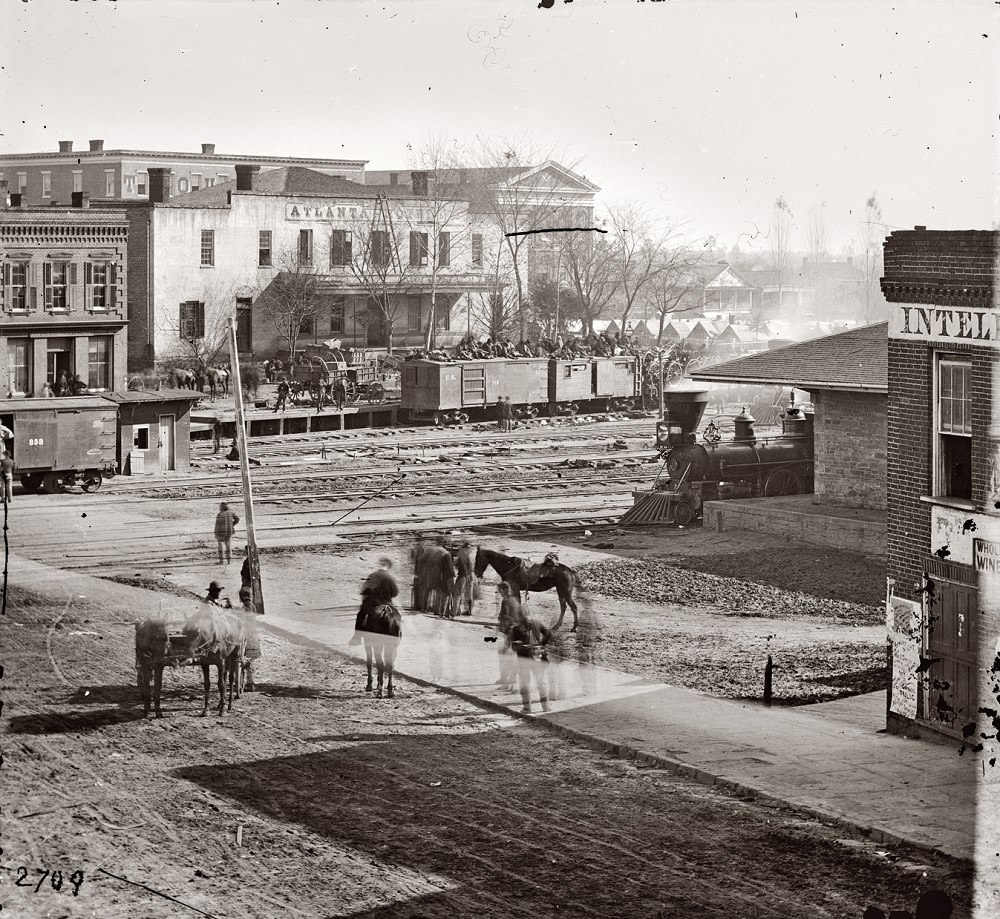 #28 Union soldiers on boxcars at railroad depot next to offices of the Atlanta Intelligencer during the city’s occupation by General Sherman