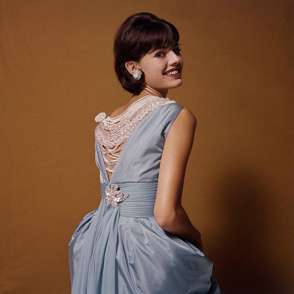 #4 Fashion Model looking over shoulder wearing blue dress which has a V shaped back, Glamour 1960
