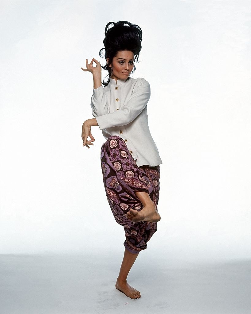 #48 Israeli actress Daliah Lavi stands in Thai Dance pose, wearing Rudi Gernreich’s white jacket, Vogue 1965
