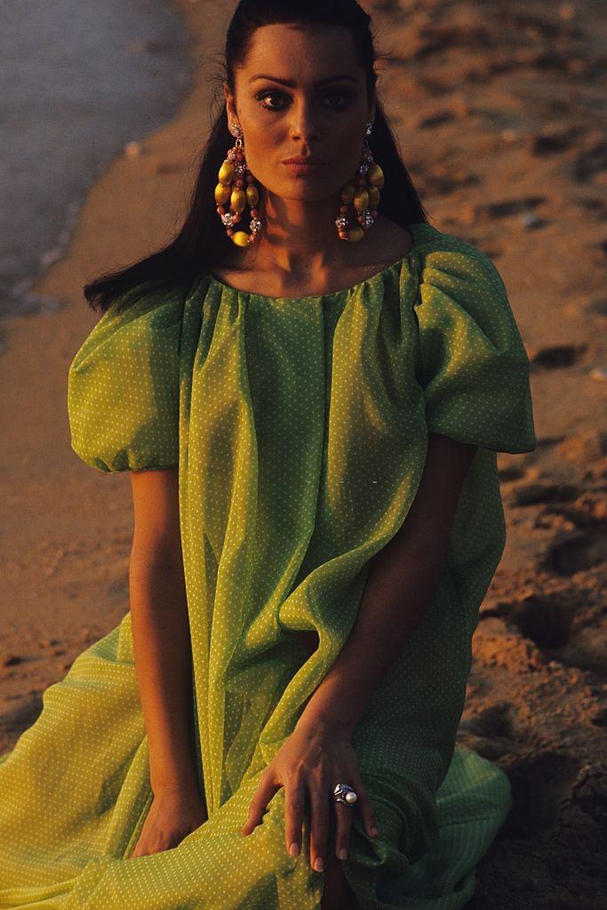 #50 Israeli actress and model Daliah Lavi kneeling on beach, wearing voluminous peignoir green with white polka dots, Vogue 1965