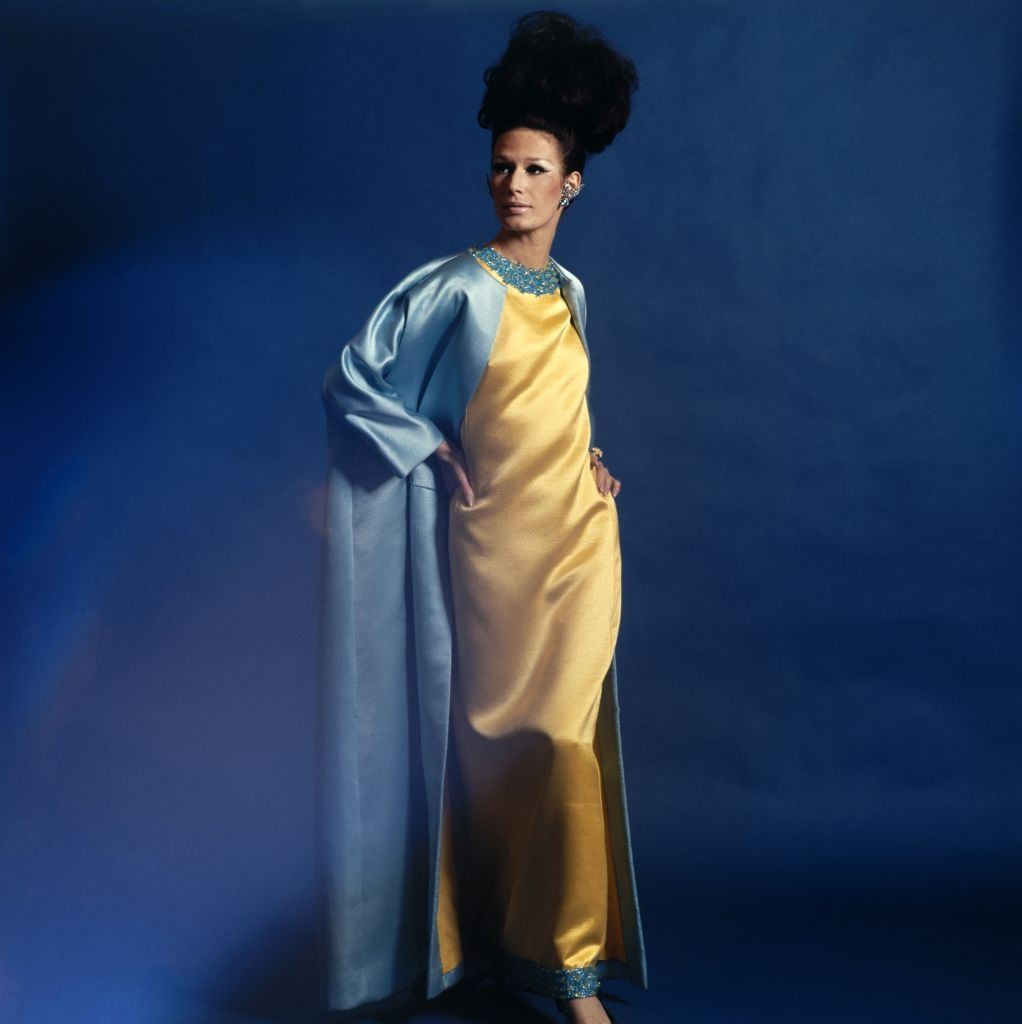 #57 Model wearing a Harold Levine blue satin coat and crystal jeweled yellow full-length dress, Vogue 1965