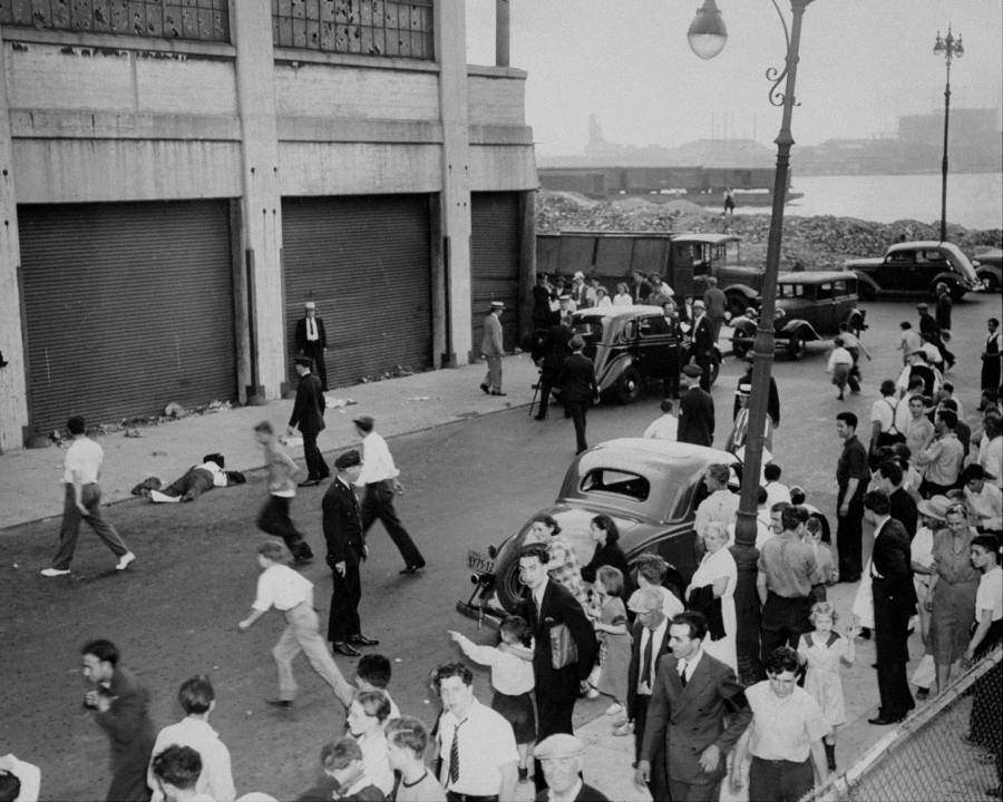 A crowd gathers around the body of John Masseria, Joe “The Boss” Masseria’s brother, as police arrive at the murder scene on 19th Street. 1937.