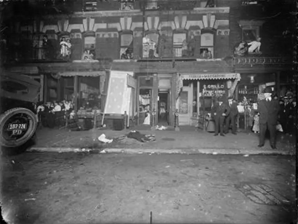 Onlookers lean out of tenement windows to view a man’s body on the sidewalk, 1916-1920