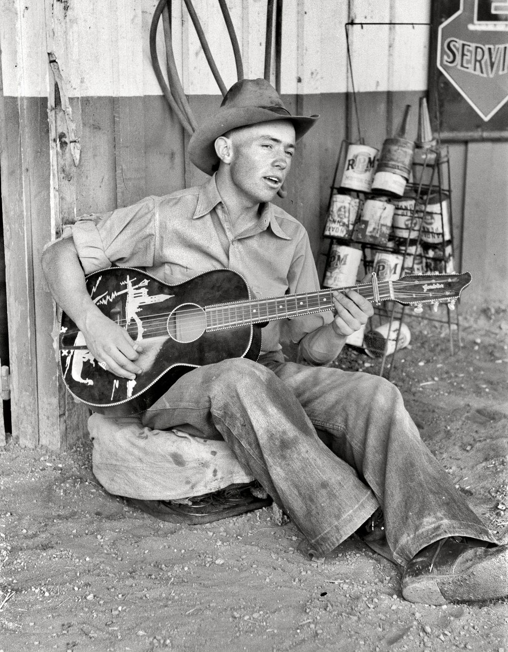 #6 Farm boy playing guitar in front of the filling station and garage, Pie Town, New Mexico, June 1940