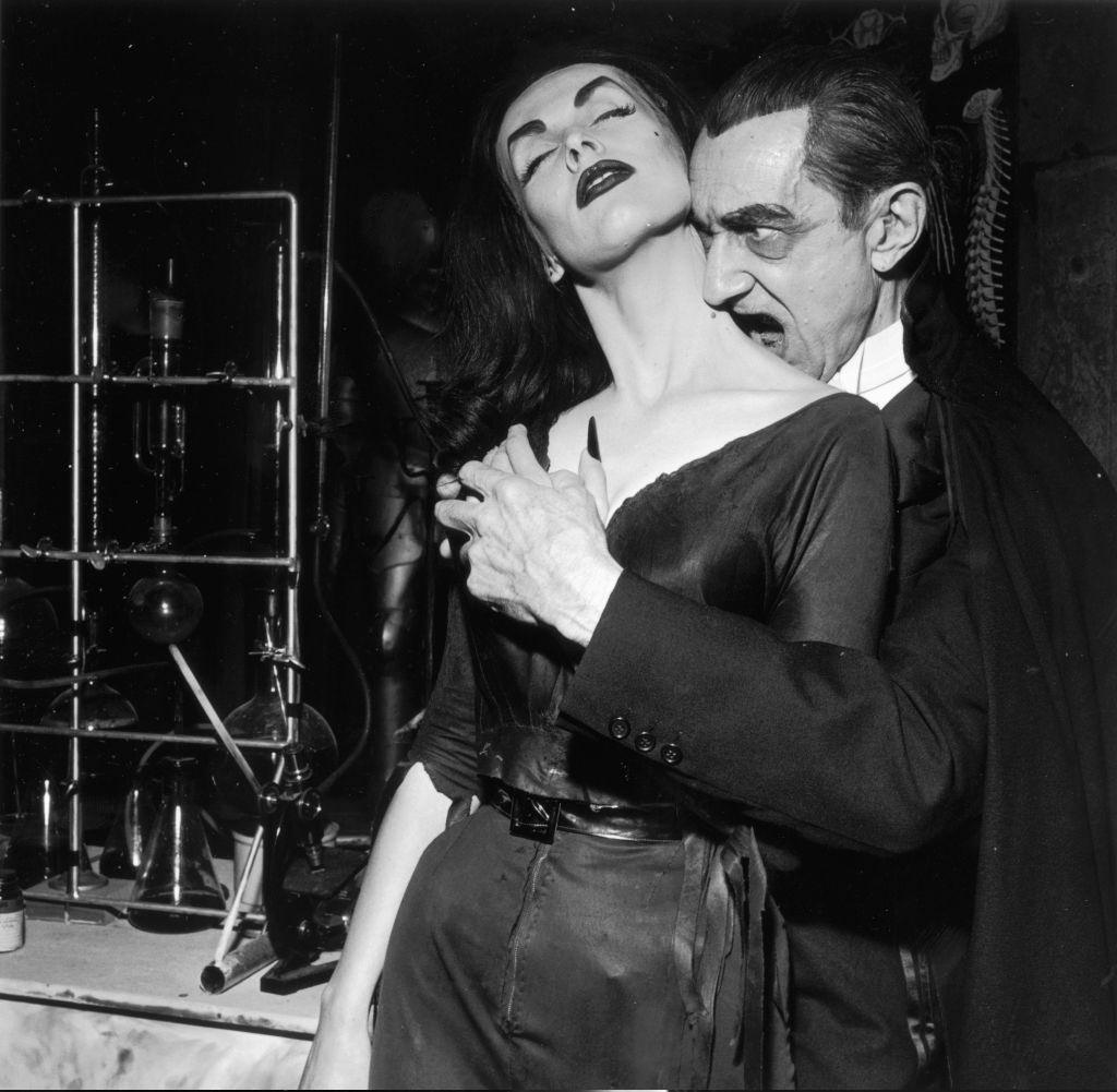 Bela Lugosi playing Dracula, prepares to bite into Finnish-born actor and television host Vampira’s neck as they clasp hands, 1956