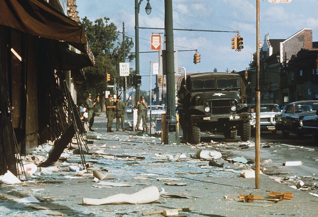 #26 National Guardsmen armed with rifles stand guard amid debris littering the streets of the West Side of Detroit, 1967