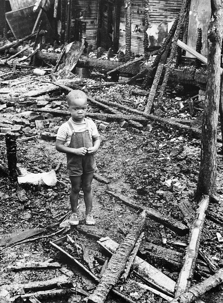 #34 Three year old Thomas Allen stands the ruins of his home on Detroit’s east side, 1967