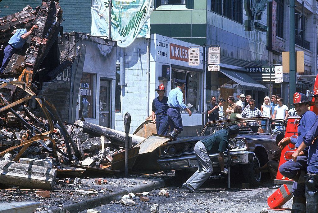 #43 A group of onlookers gather to watch authorities clean up debris after fires during riots in Detroit, 1967