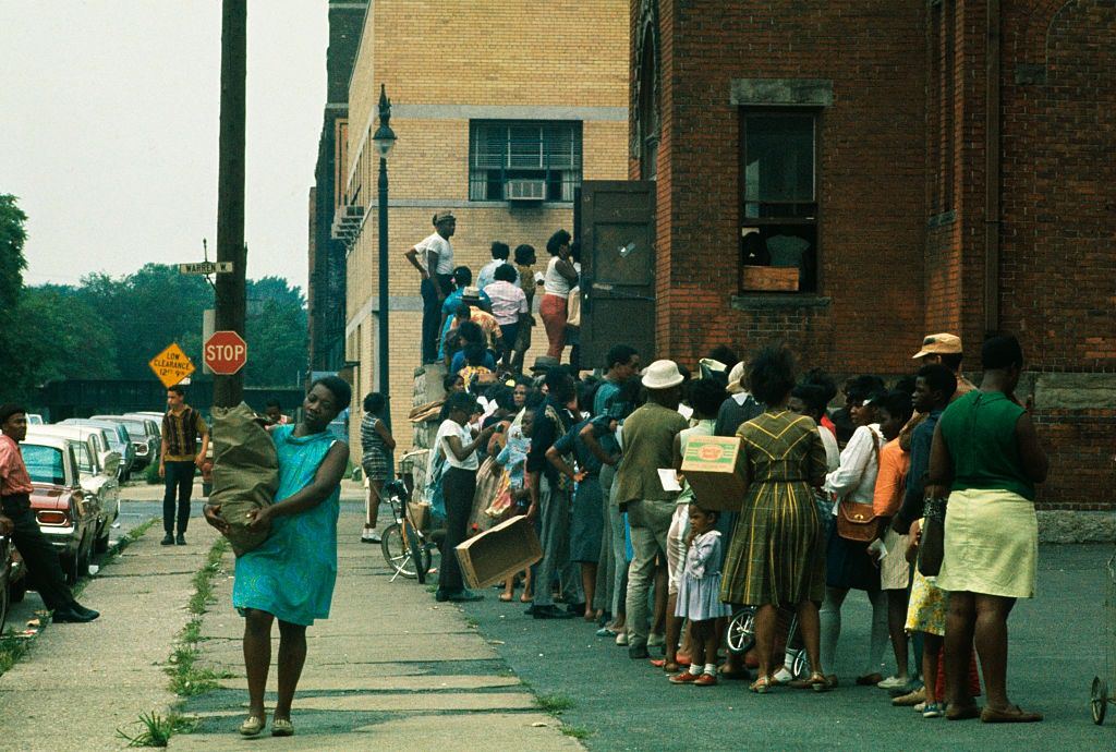 #44 Residents of this riot-torn area, some holding empty cardboard boxes, line up outside building where food and clothing is being distributed, 1967