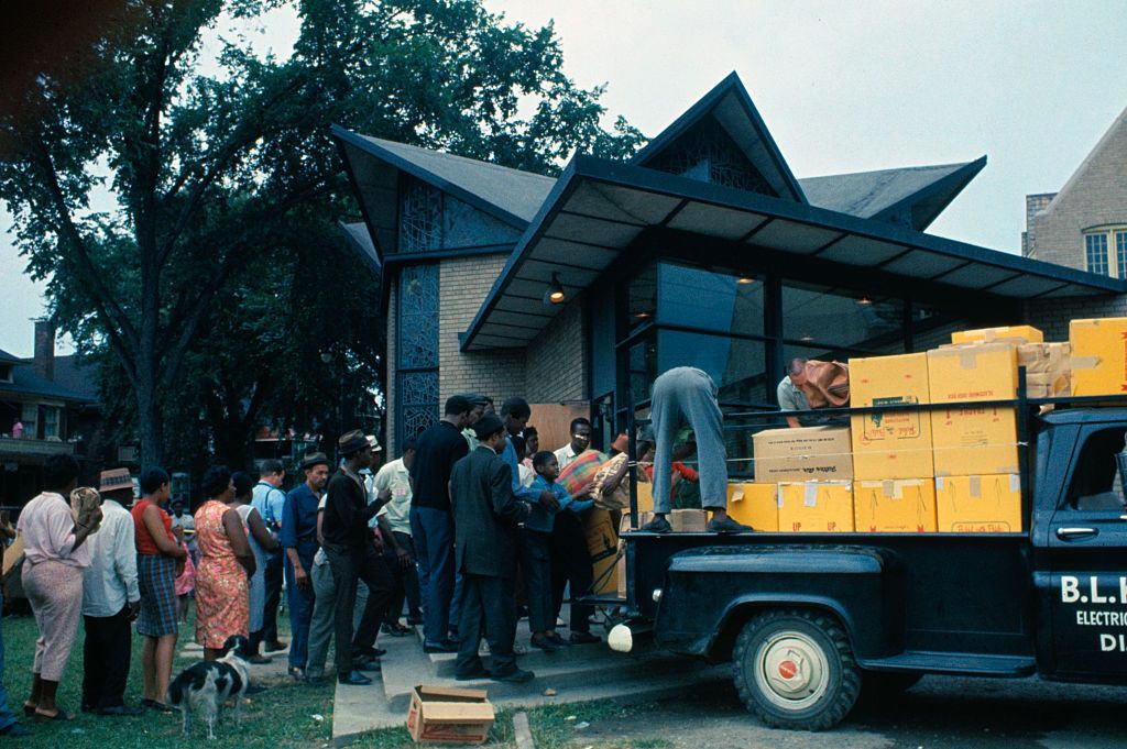 #45 Residents of this riot-torn area, some holding empty cardboard boxes, line up outside building where food and clothing is being distributed, 1967