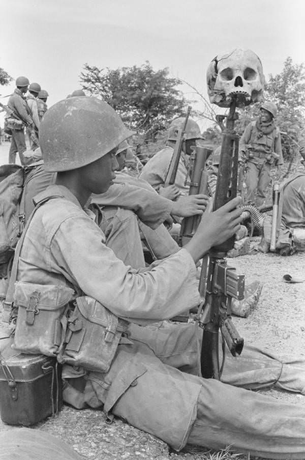 #16 A child soldier with a human skull resting on the tip of his rifle, Dei Kraham, Cambodia. 1973.