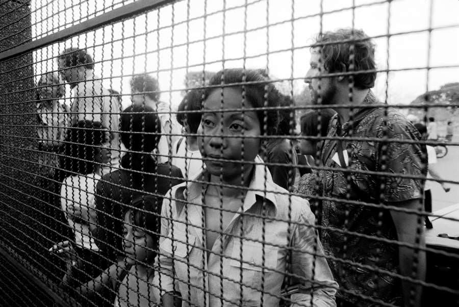 #19 Refugees peer through the gate to the French Embassy, begging to get in, Phnom Penh. 1975.
