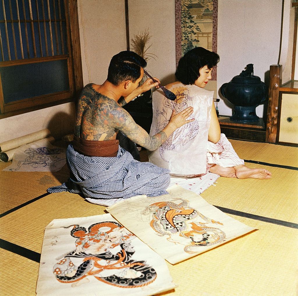 #21 Japanese tattoo artist, Tokumitsu Uchida, with water brush, transferring picture chosen by customer as first step in tattooing design, 1955