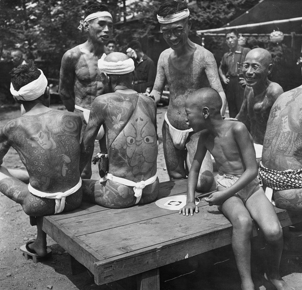 #22 A young boy admires the tattoos on the backs of Japanese men at a rally held for tattooists and their clients to show off their ‘designer’ bodies, 1958