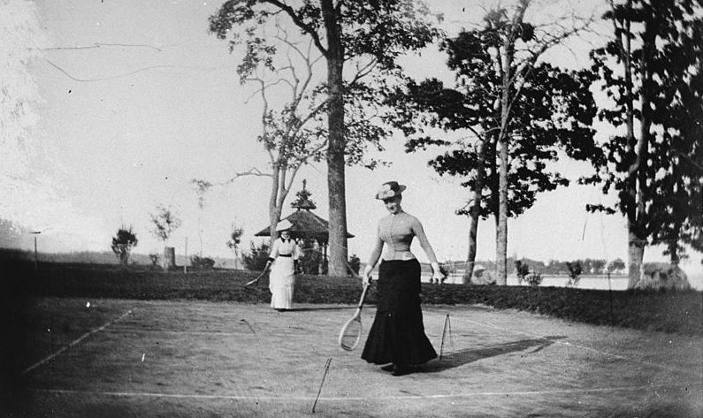 #22 Two well-dressed women playing lawn tennis next to a lake, New York, 1880s
