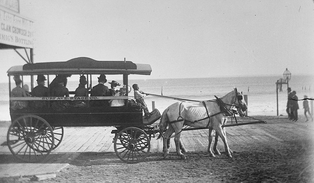 #23 A young black boy pulling the reins of a horse drawn coach owned by the Surf Ave. Stage Co., alongside the boardwalk at Coney Island, 1884