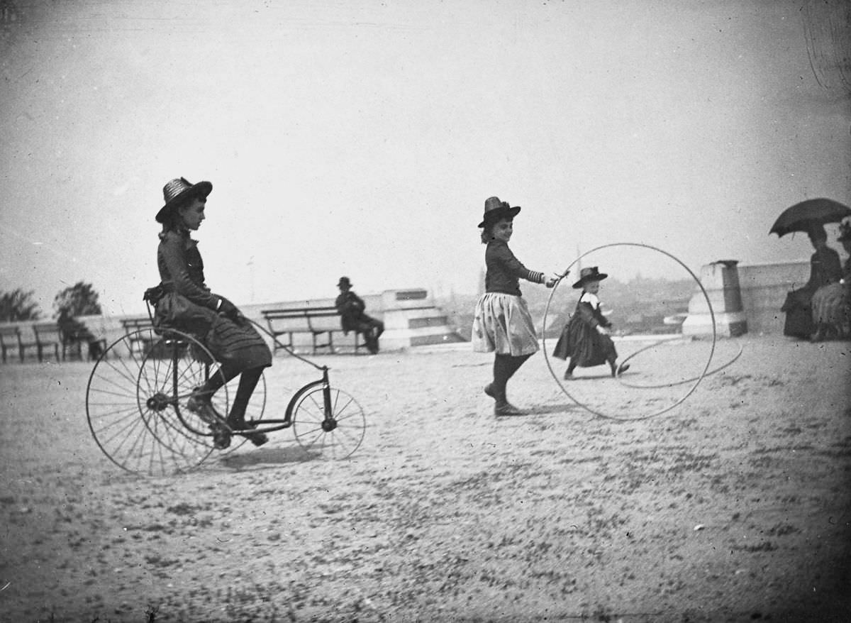 #11 Isabel Harter rides a tricycle while her sister Nellie rolls a hoop in Fort Greene.May 22, 1886