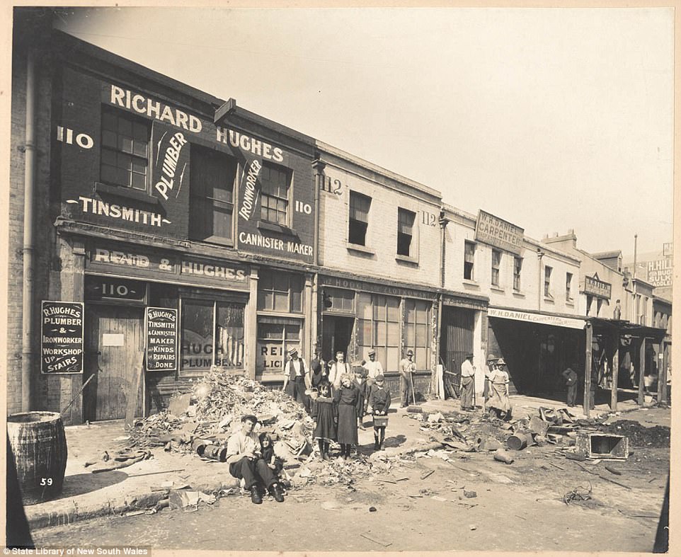 People on the side of Sussex Street outside a workshop for a tinsmith and cannister maker in Sydney during a quarantine period, taken sometime in the early 1900s