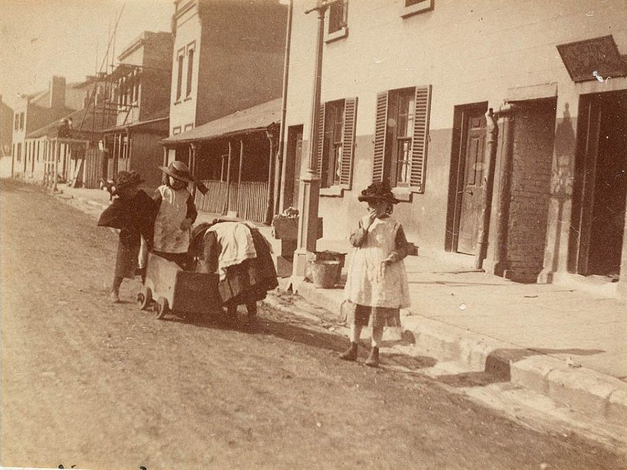 #16 Four children playing in the street in Sydney with a little wooden cart, wearing dresses and hats with ribbons, circa 1885-1890.