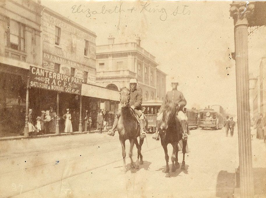 #37 Men on horseback have been photographed at the corner of King and Elizabeth Street in Sydney in 1890, as women watch on from the side of the street and trams go past in the background
