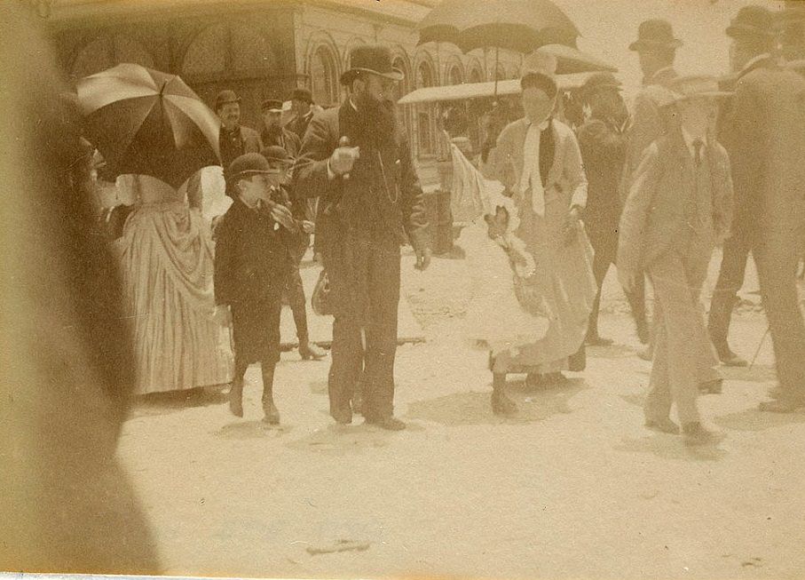 #19 A group of people is seen walking through the streets of Sydney circa 1885-1890, with the men and boys wearing top hats and suits and the women in long dresses carrying umbrellas