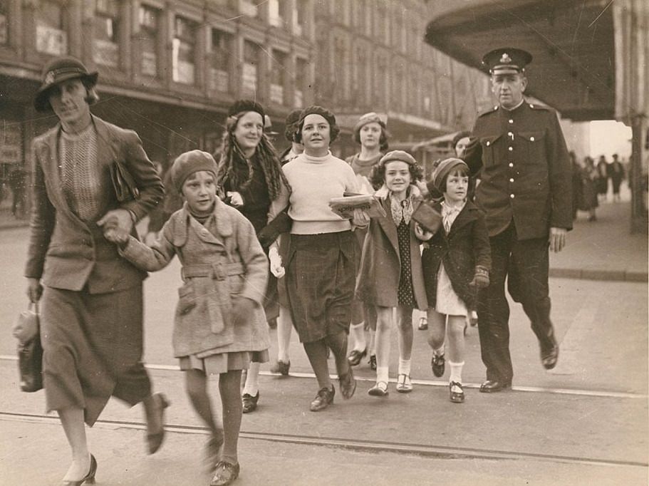 #7 Women and children are seen being escorted across the road by an officer in uniform in Sydney, circa 1940