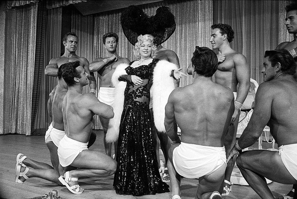 #48 Entertainer Mae Westmaking her nightclub debut with loin-clothed dancers at Hotel Sahara, Las Vegas, 1951.