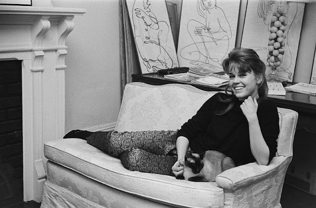 #23 Jane Fonda smiling while lying on the sofa with her Siamese cat at her home.