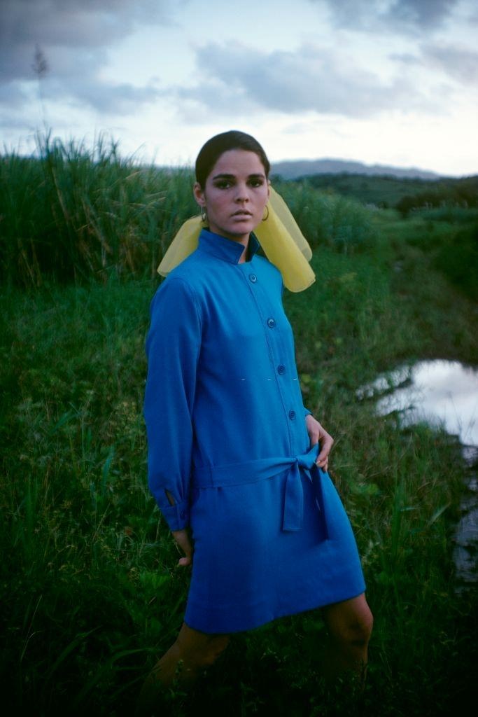 #13 Ali MacGraw standing in a field modeling a blue belted shirtdress, 1968.
