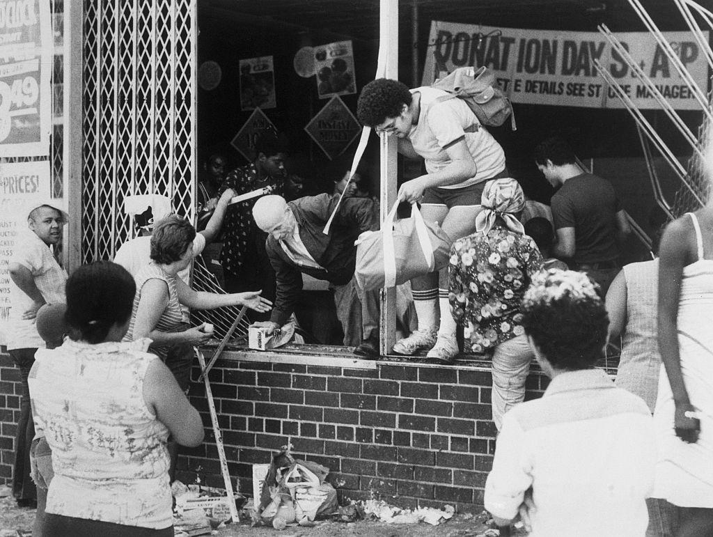 #13 Looters, young and old, leave an A & P supermarket at Ogden Avenue and 166th Street in the Bronx through a broken window, New York, New York, 1977.