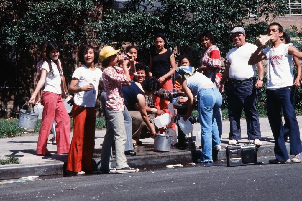 #42 People fill up buckets and bottles from an opened fire hydrant after the blackout, New York City, 1977.