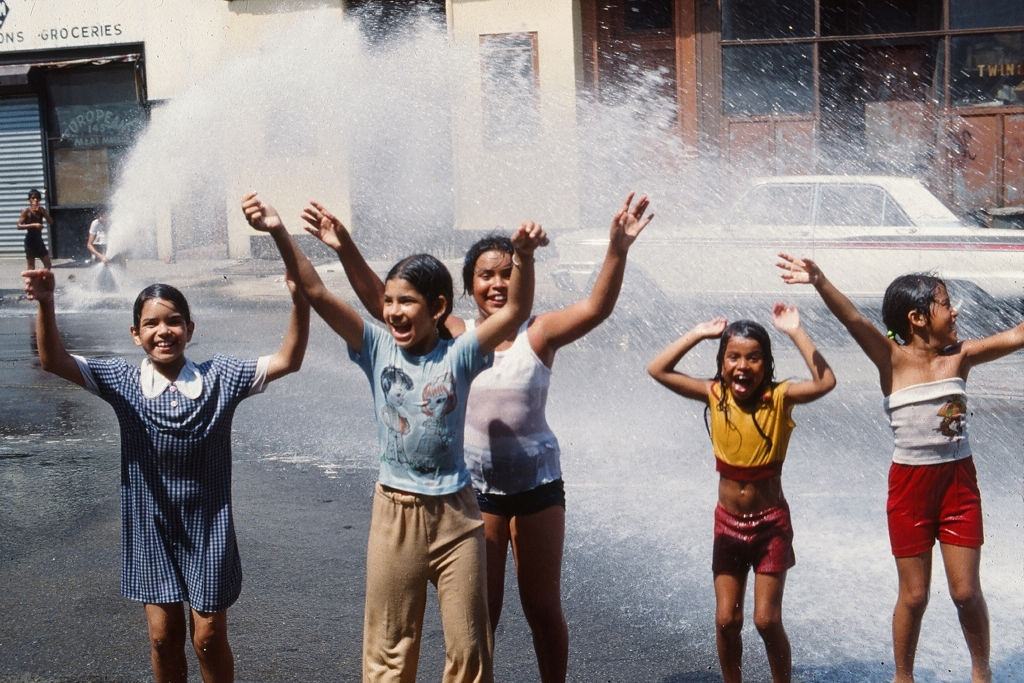 #21 A group of young girls play in the water from an opened fire hydrant after the blackout of 1977.