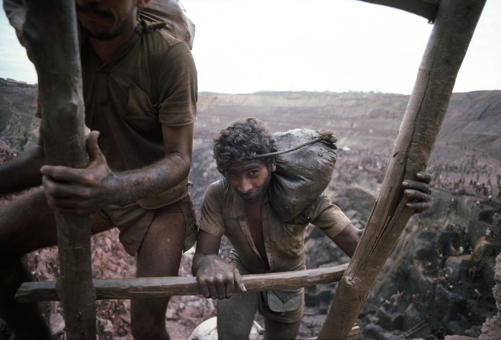 #24 Mine workers use a wooden ladder to carry out 40-pound bags of ore, Serra Pelada, Brazil.