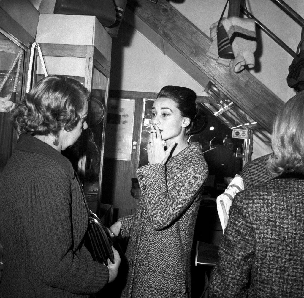 #43 Audrey Hepburn smoking a cigarette and talking to a woman in a leather shop. Rome, 1950s.