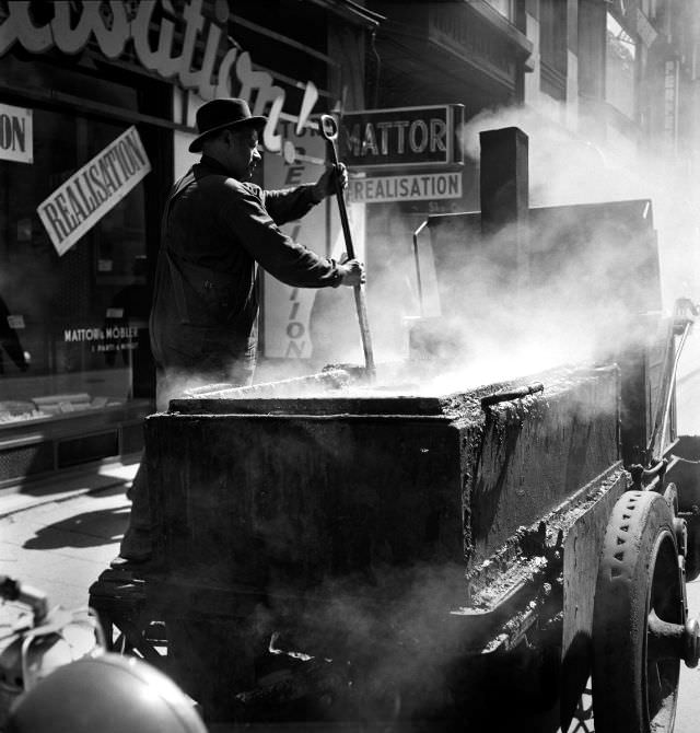 #23 A road worker stirs boiling asphalt on Drottninggatan street.