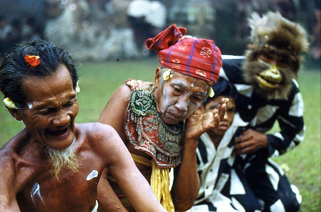 #9 A devotee goes into a trance watched by an elderly man with a painted face and a man wearing a monkey mask, 1956.