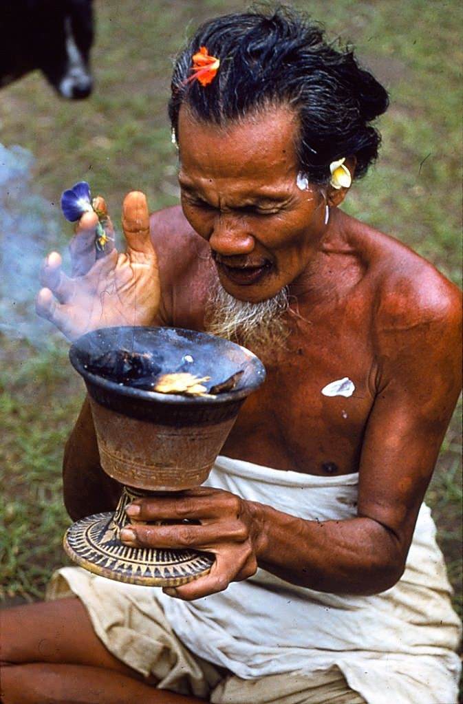 #26 A Balinese man holds a cup and inhales fumes from the smoking ashes within, 1956.