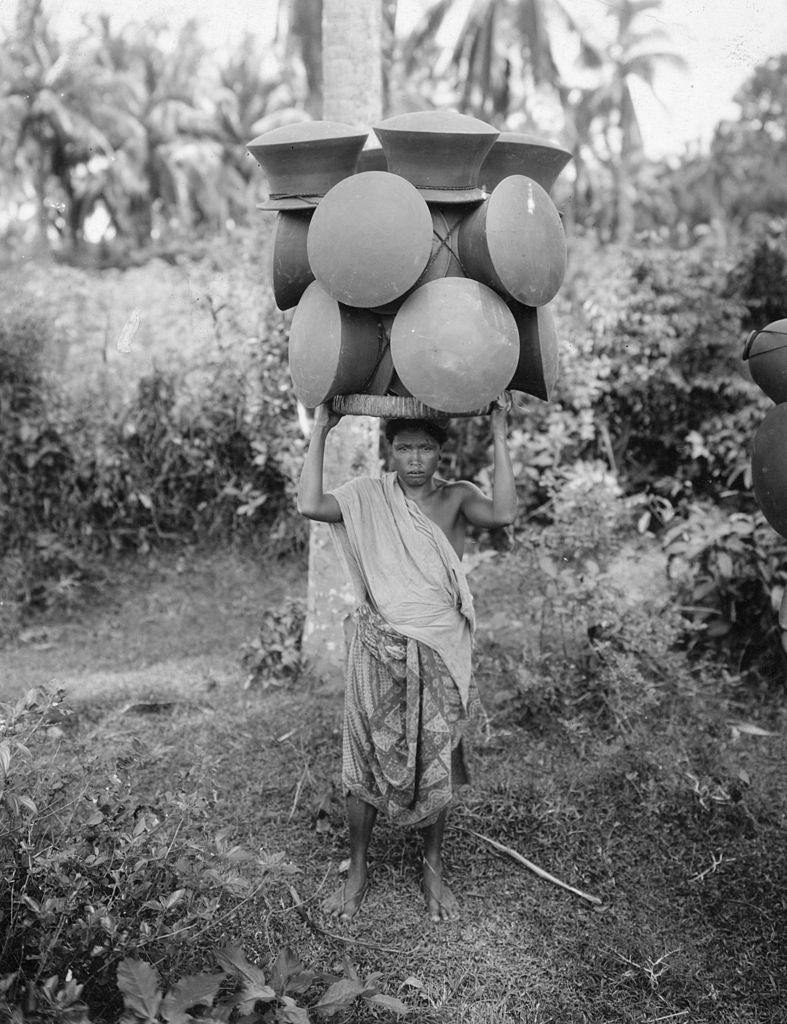 #29 A woman balancing hand made clay pots on her head to carry them hundreds of miles to market. Bali, 1955