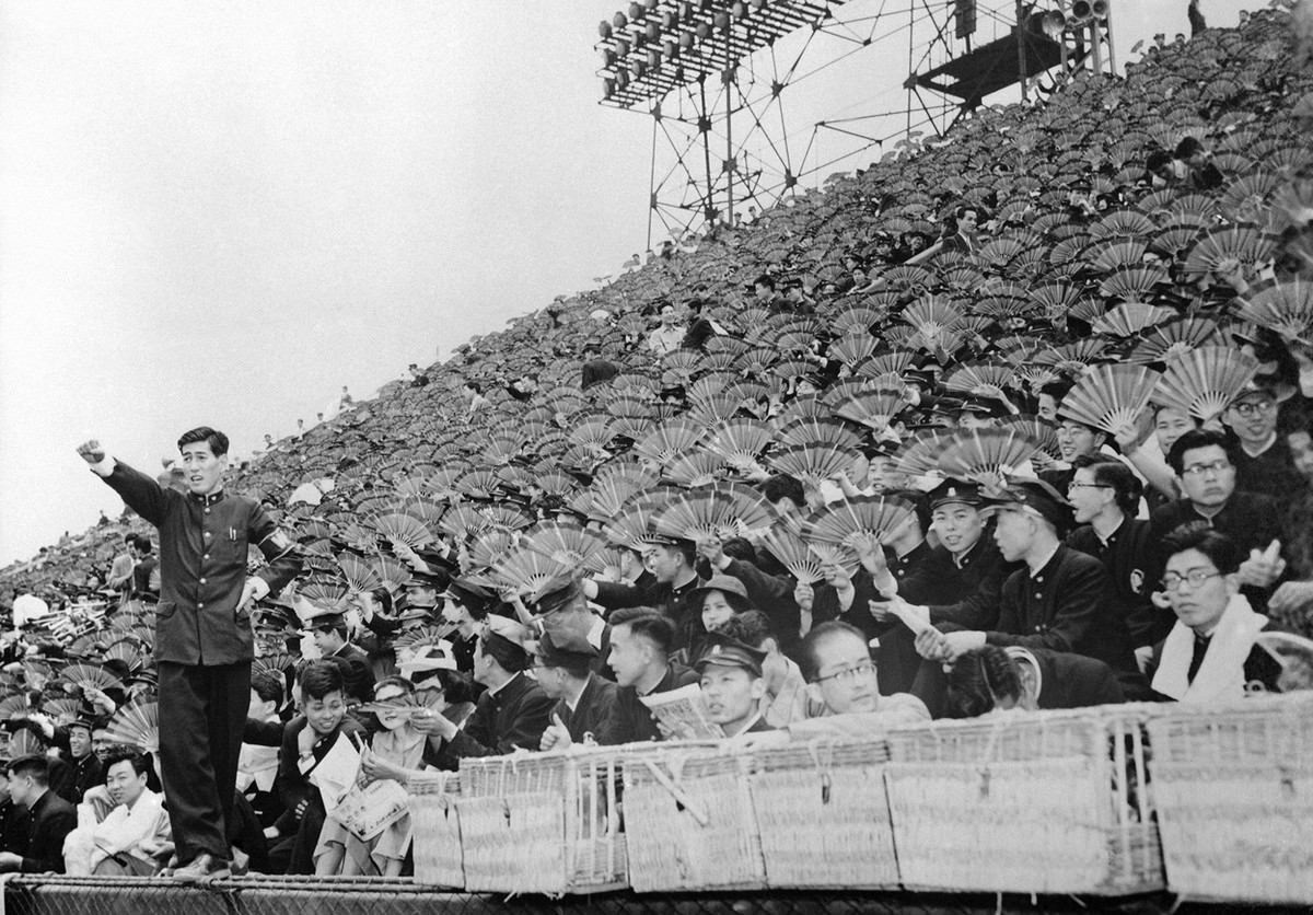 #20 Spectators equipped with fans watch a baseball game between Waseda and Keio Universities at Meiji Park, Tokyo, on June 1, 1954.