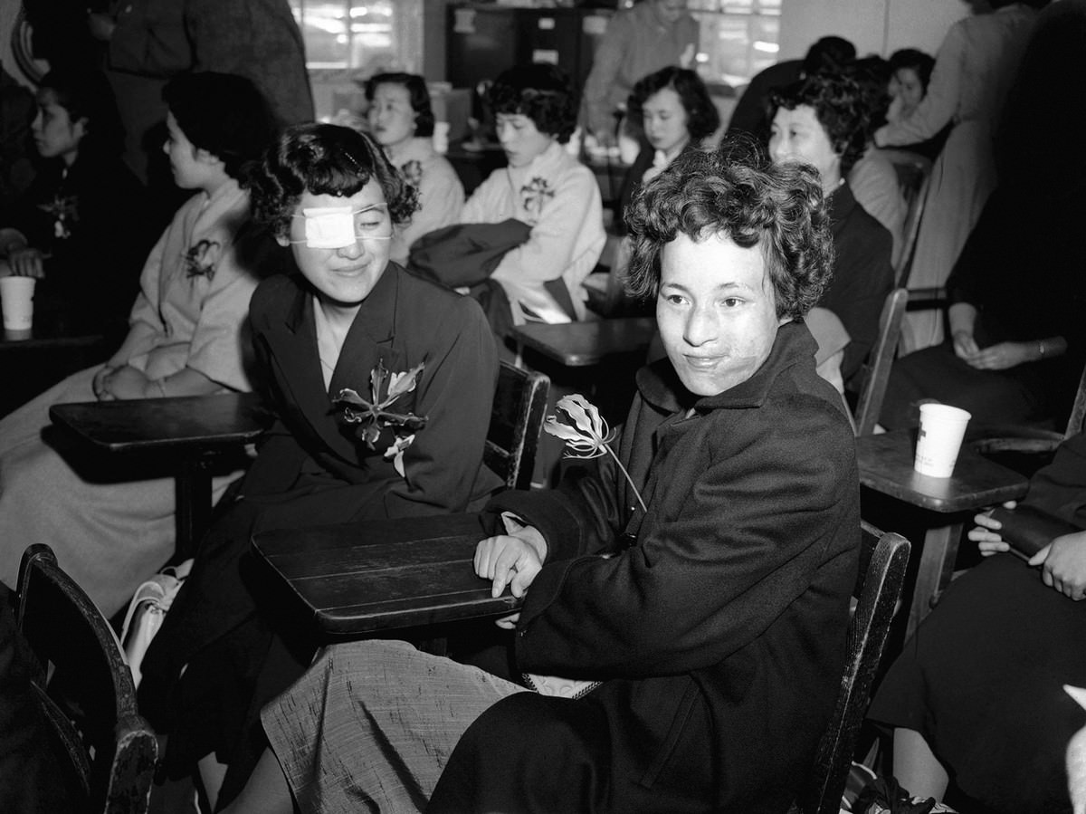 #25 Japanese girls Mitsuko Kuranoto, left, and Emiko Takemoto, survivors of the Hiroshima atomic bombing 10 years earlier, face newsmen and photographers at the Mitchel Air Force base on Long Island, New York, on May 9, 1955.