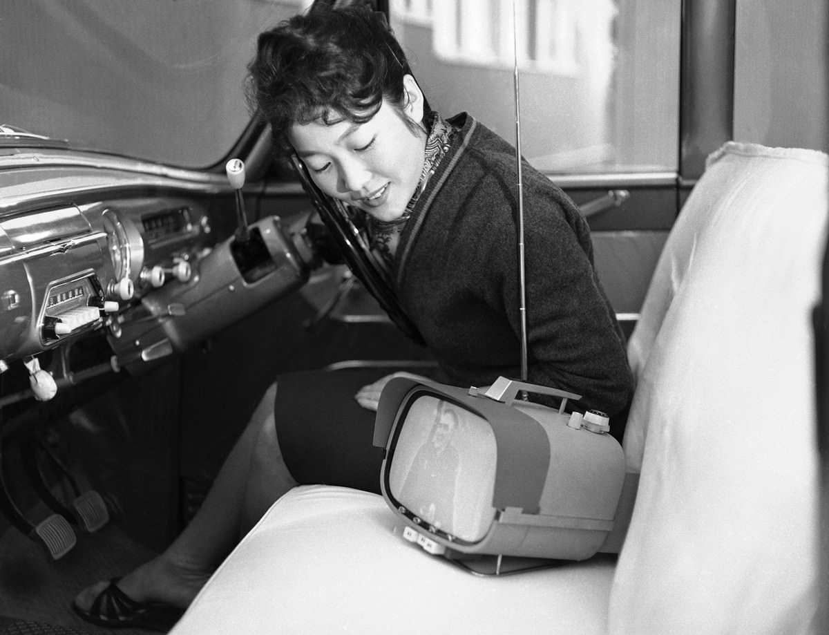 #36 Tomiko Kawabata sits in her car and admires her new all-transistor, portable television set which Sony put into mass production, in Tokyo, on January 5, 1960.
