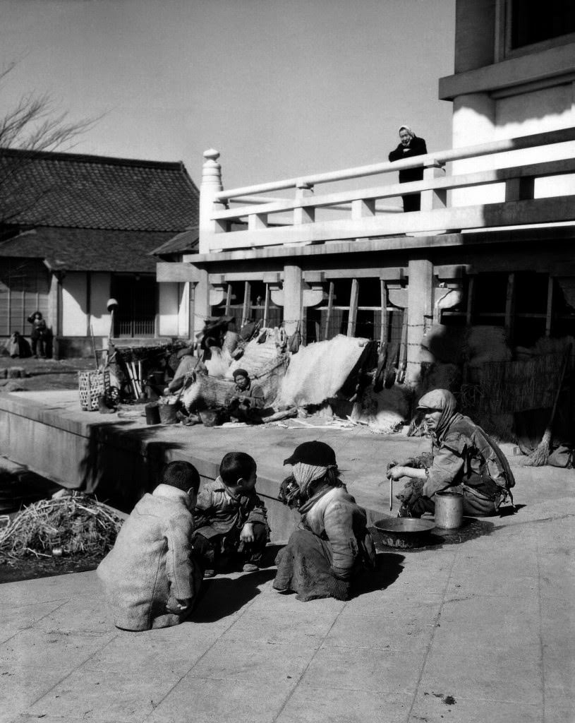 #46 Near the railroad station a group of unfortunate Japanese squatters all bundled up in rags sit in front of their make-shift homes