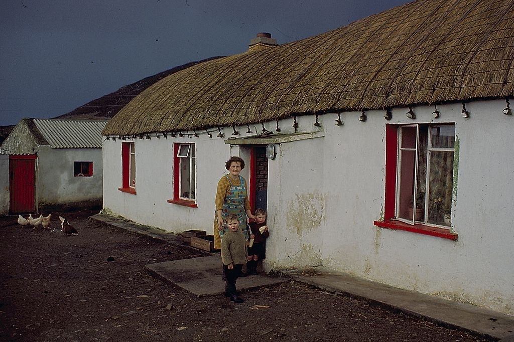 #10 A woman stands with two small boys in front of a thatched cottage in County Donegal, Ireland in 1968.