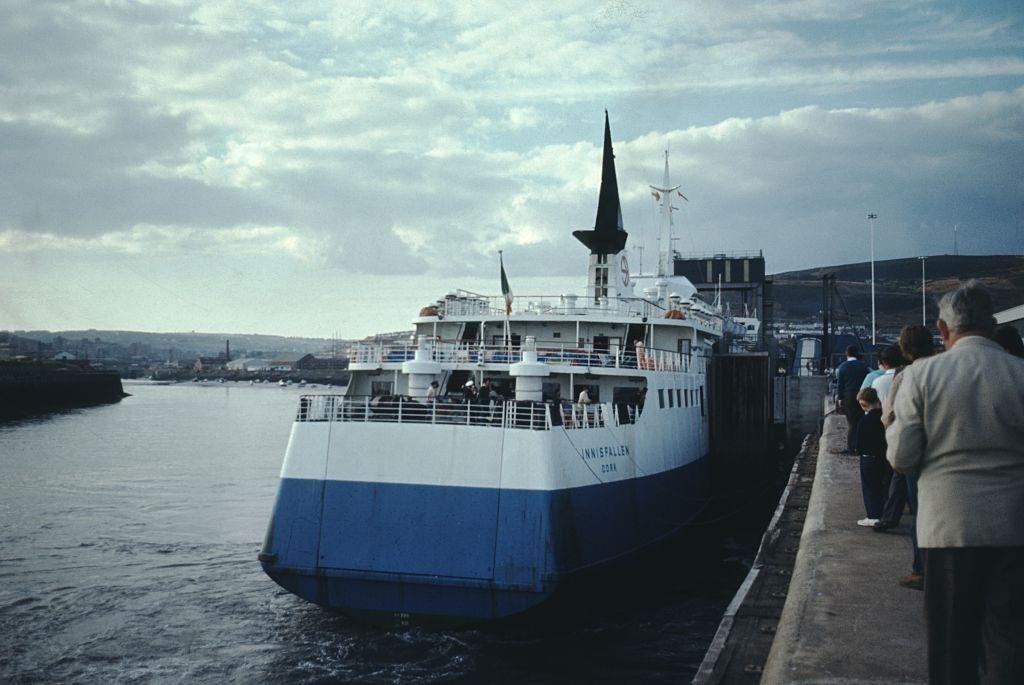 #20 Ferry to Innisfallien pulling up to a dock, tourists preparing to embark, on a dreary, overcast day, Ireland, 1960.