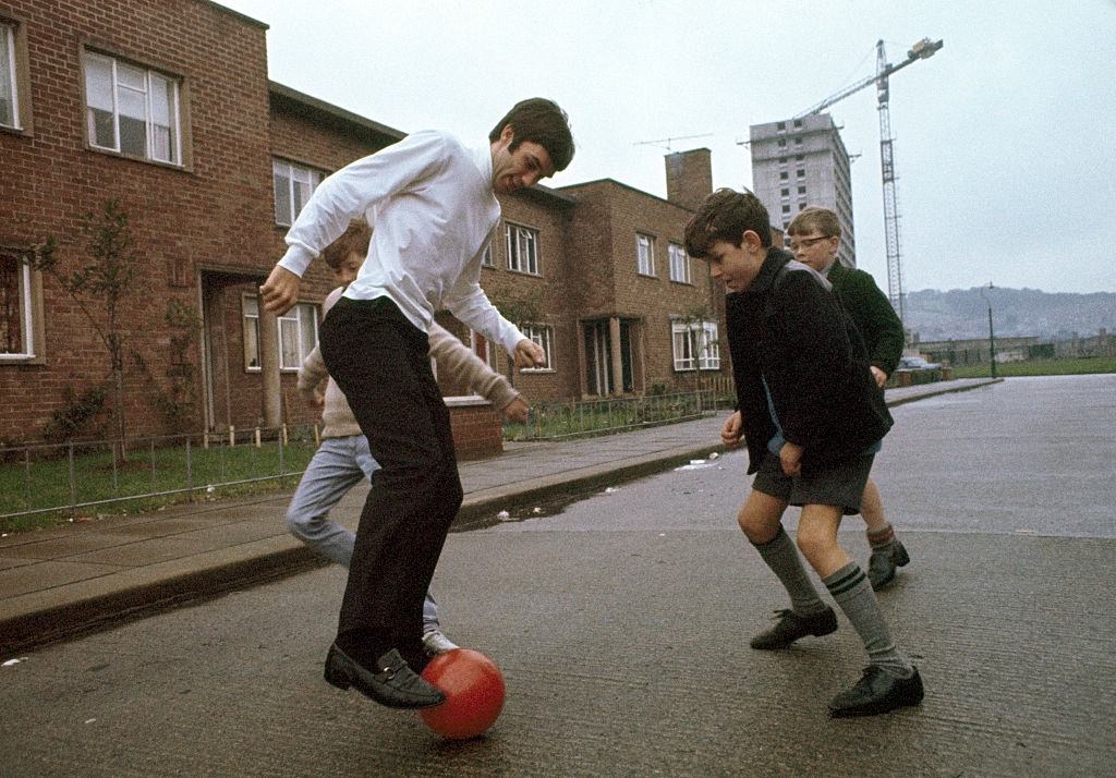 #29 Manchester United footballer George Best playing football in the street with some local boys near his family’s home in Belfast, Northern Ireland, circa 1967.