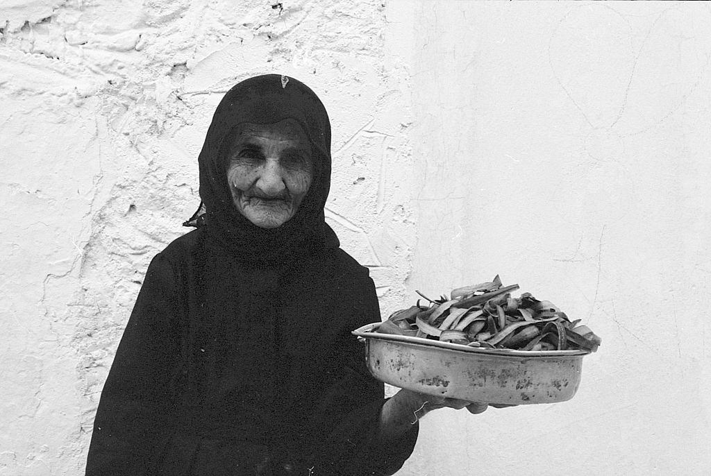 #12 An old woman with a pot full of pods. Greece, 1970s.