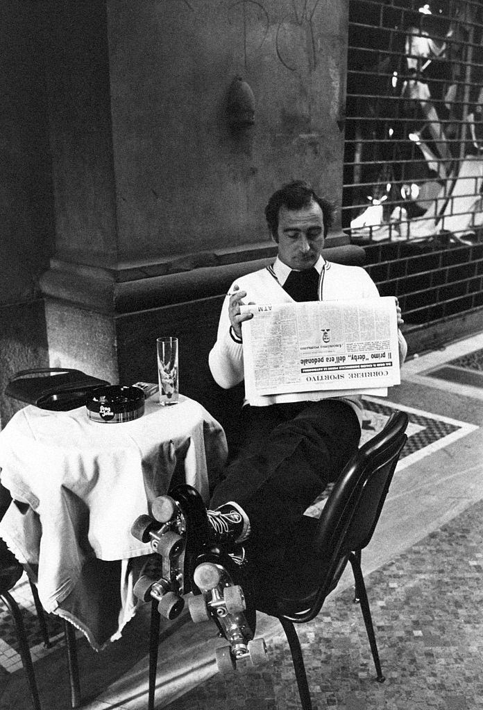 #12 A man in roller skates reading a page from Corriere sportivo seated at the table in a caf on the first Italian walking sunday due to the oil crisis. Milan, 2nd December 1973